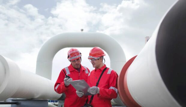 Two engineers having a discussion in front of pipes at a gas storage plant