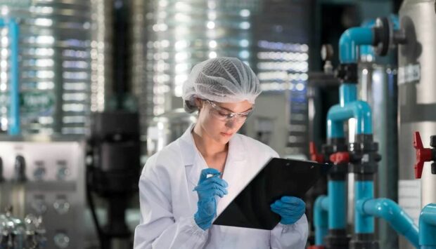 Technician reviewing data on a clipboard next to a water tank in a factory